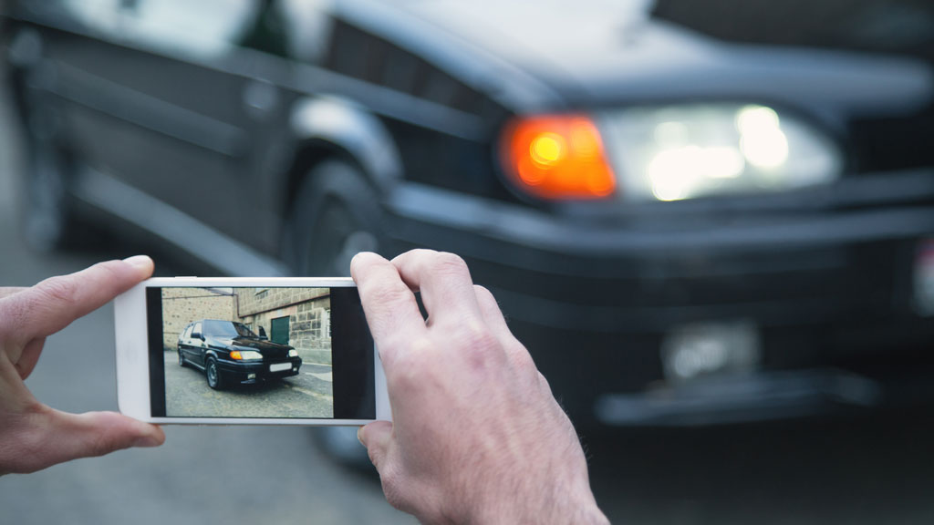 Agent de location photographiant une rayure sur véhicule avec tablette